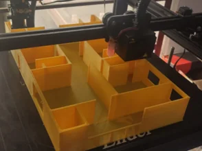 Yellow compartmented tray on a 3D printer bed beneath the printhead